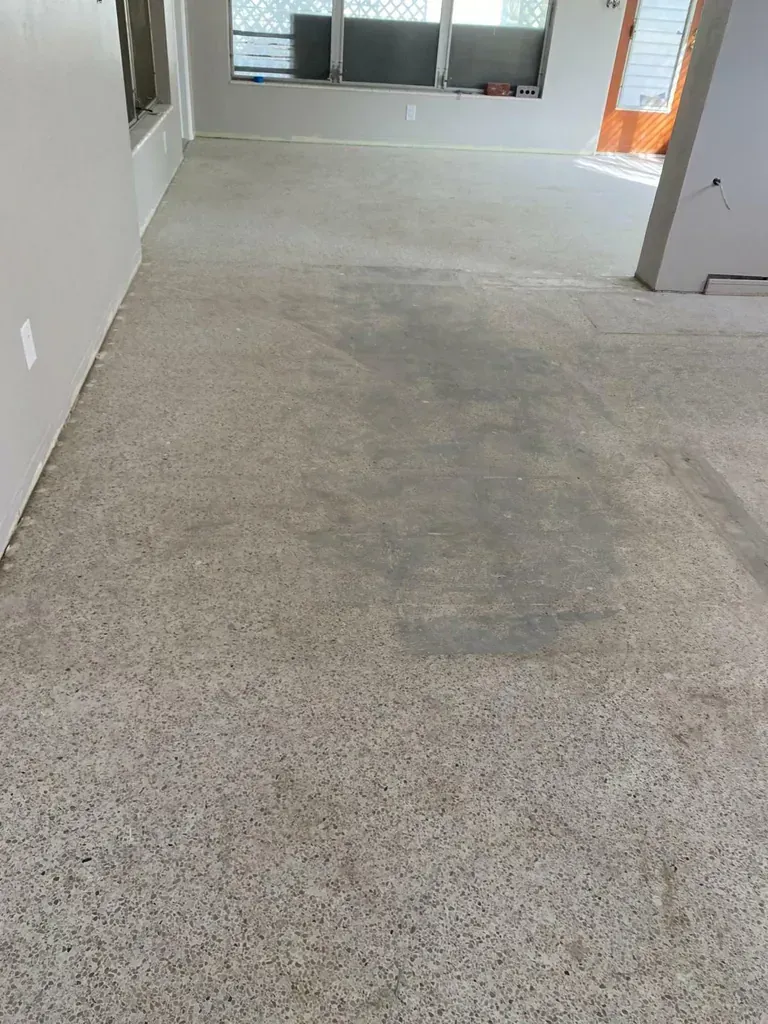 Gray concrete floor in a room under construction. Light comes in from a window.