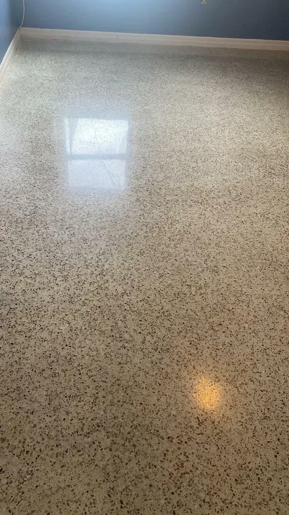 Polished concrete floor with dark aggregate; light reflects from window and light fixture.