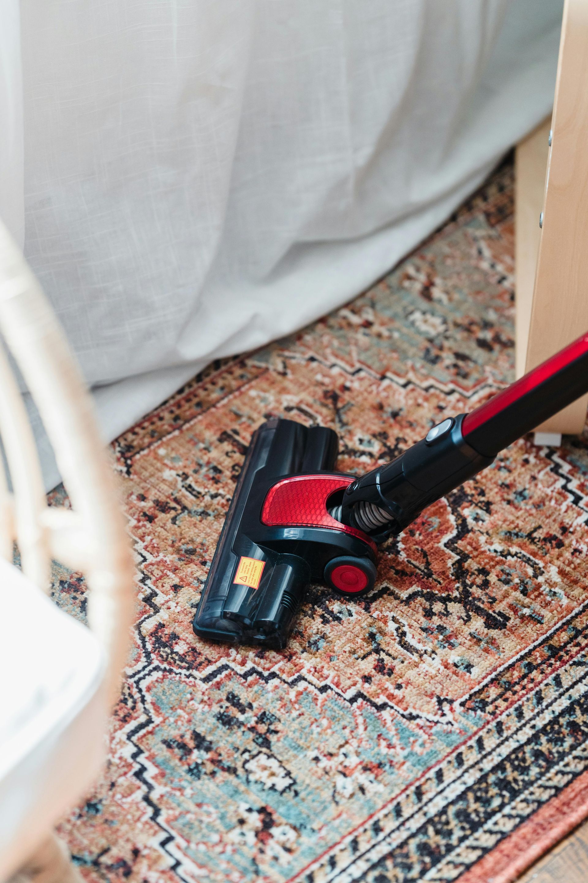 Vacuum cleaner cleaning a patterned rug near a chair and curtain.