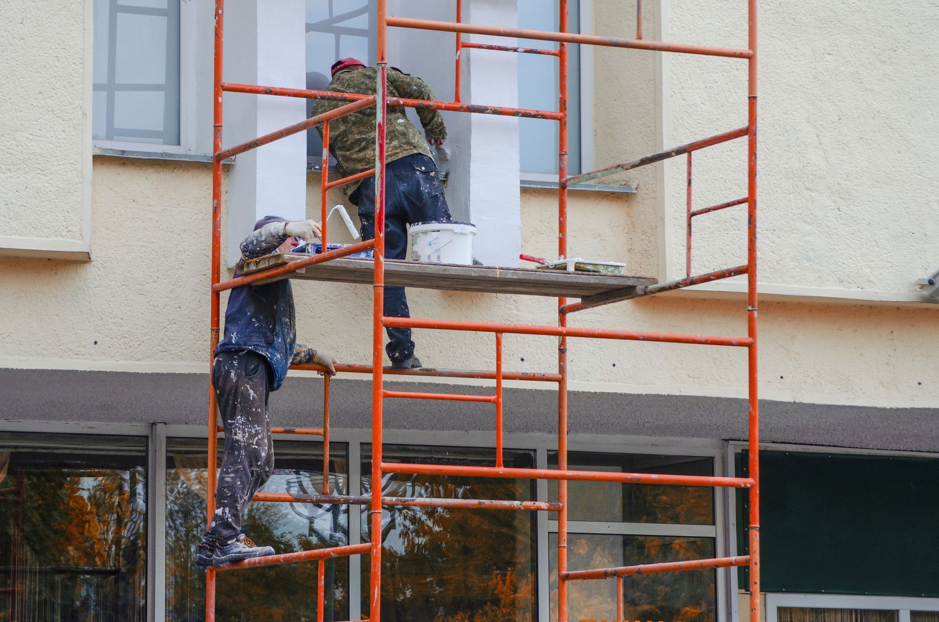 Two men are painting a building on a scaffolding.