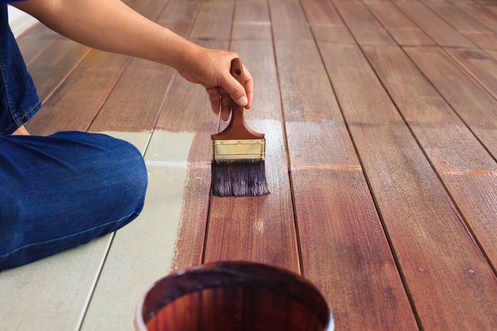 A person is painting a wooden floor with a brush.