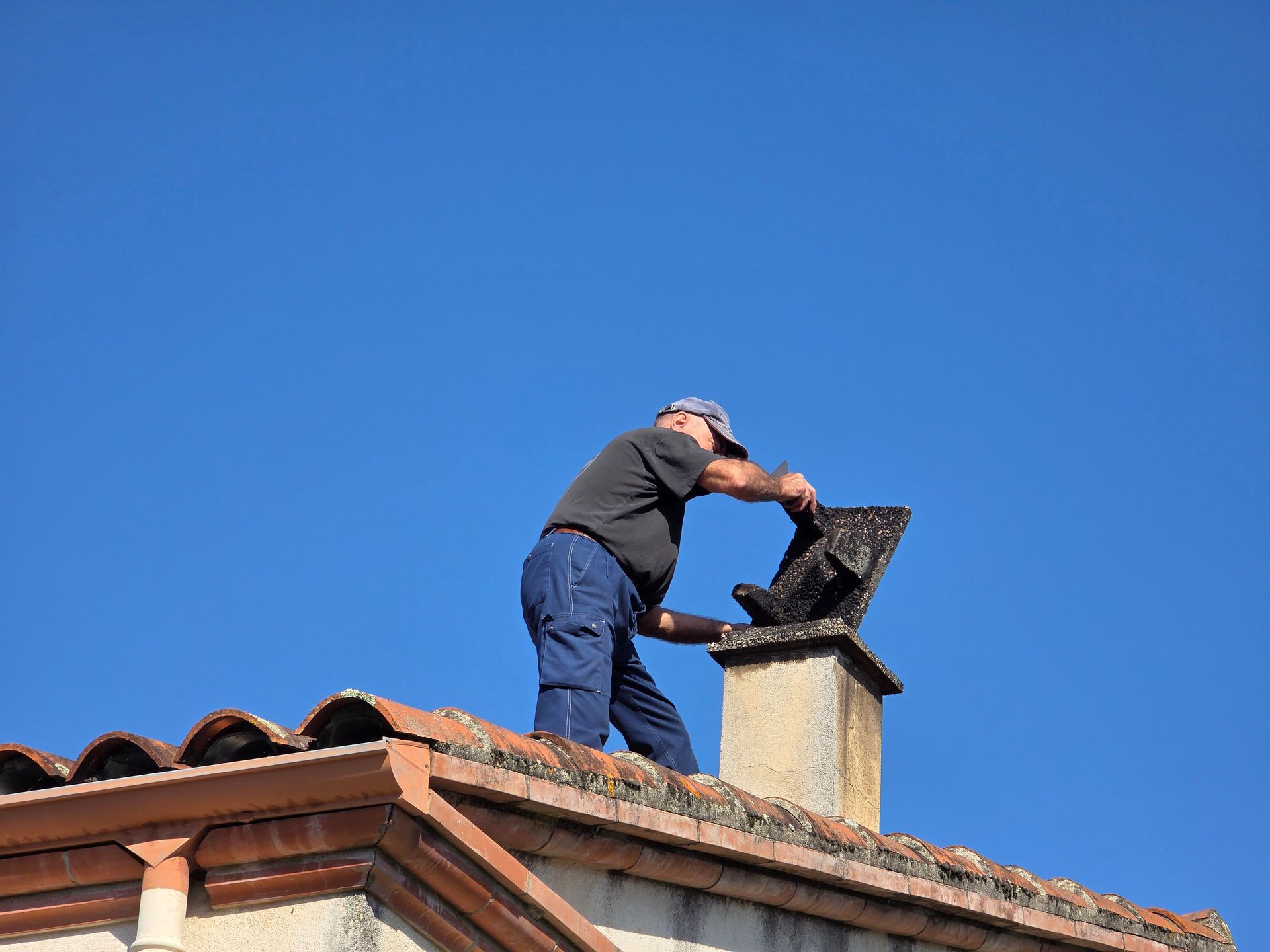 Worker inspecting or repairing a chimney cap on a tiled rooftop under a clear blue sky. Worker inspecting or repairing a chimney cap on a tiled rooftop under a clear blue sky.