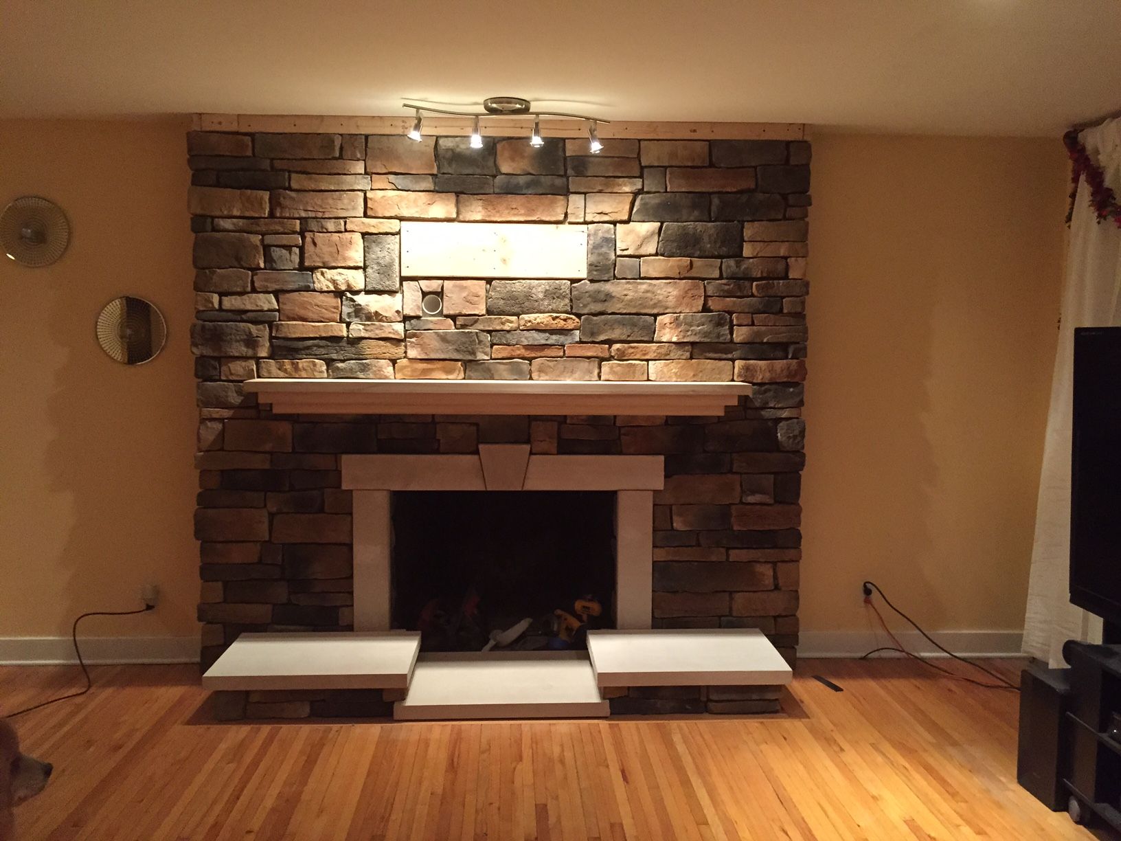 Fireplace with stone facade, light wood mantel, and matching hearth. Overhead track lighting.