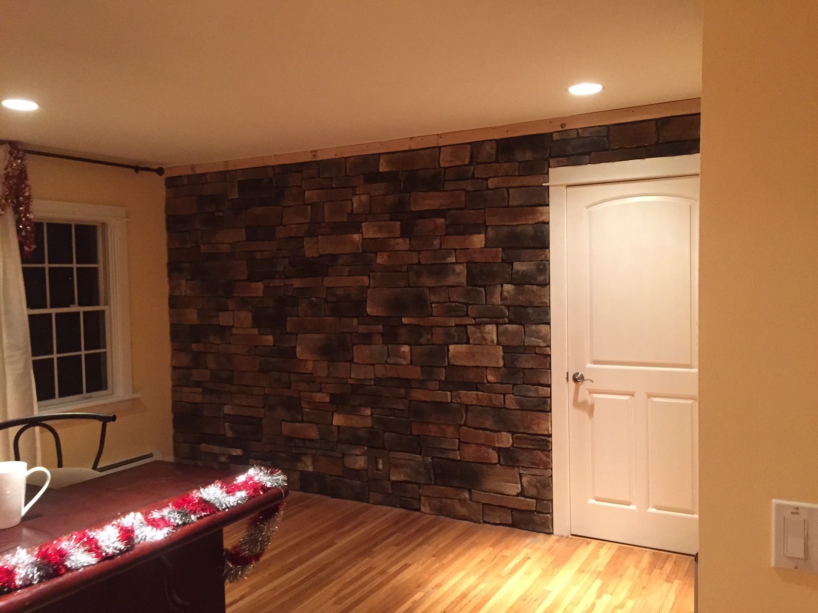 Stone accent wall with white door and wood floor in a room with warm lighting.