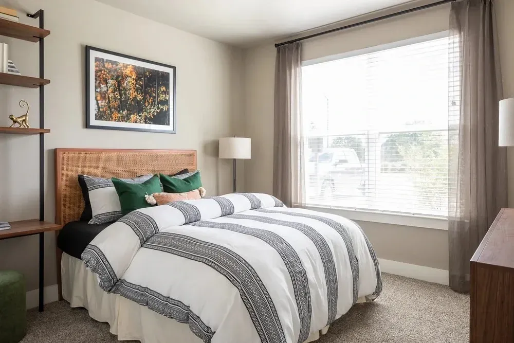 Cozy bedroom with a bed, decorative pillows, and natural light from a window.