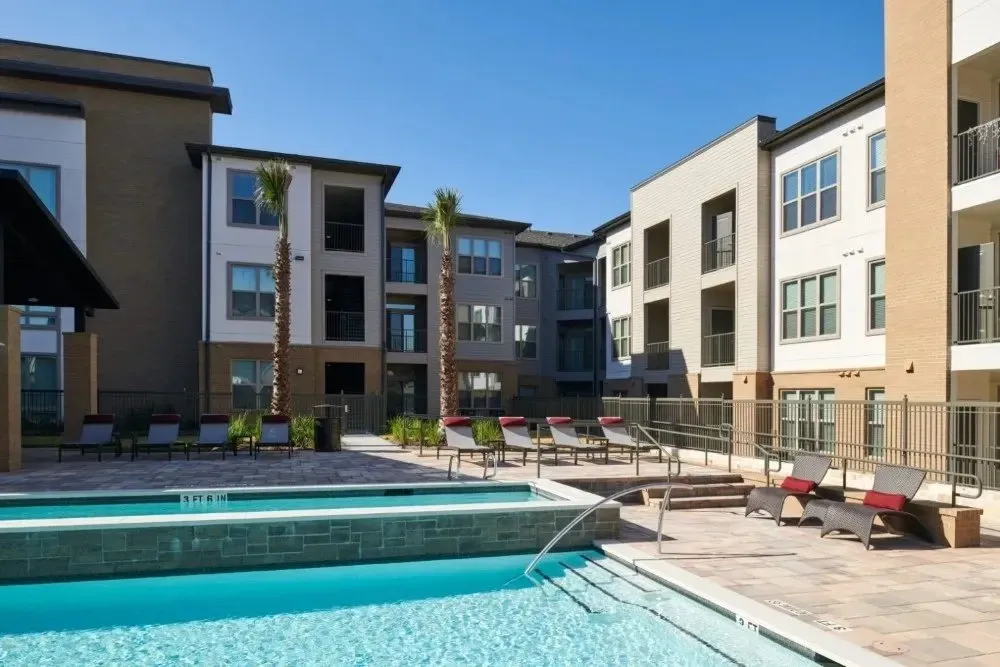 Swimming pool area surrounded by palm trees and apartment buildings.