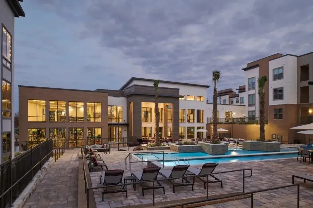View of a community pool area with lounge chairs and palm trees during twilight.