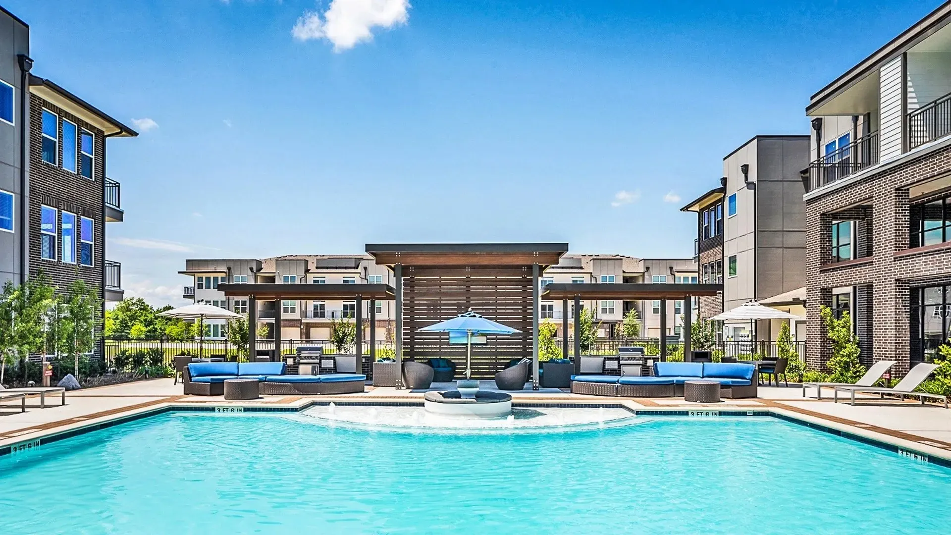 View of a community pool area with seating and trees under a blue sky