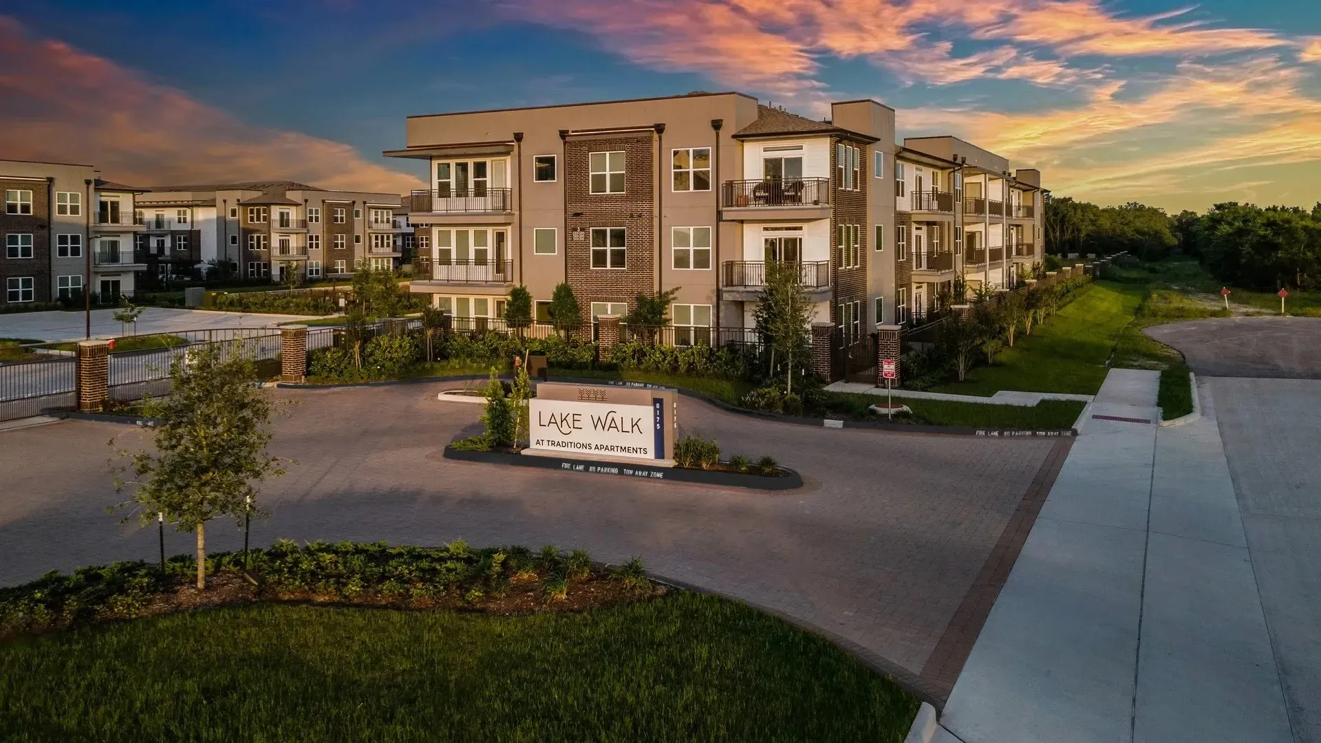 Exterior view of Lake Walk at Traditions Apartments with signage and landscaping.
