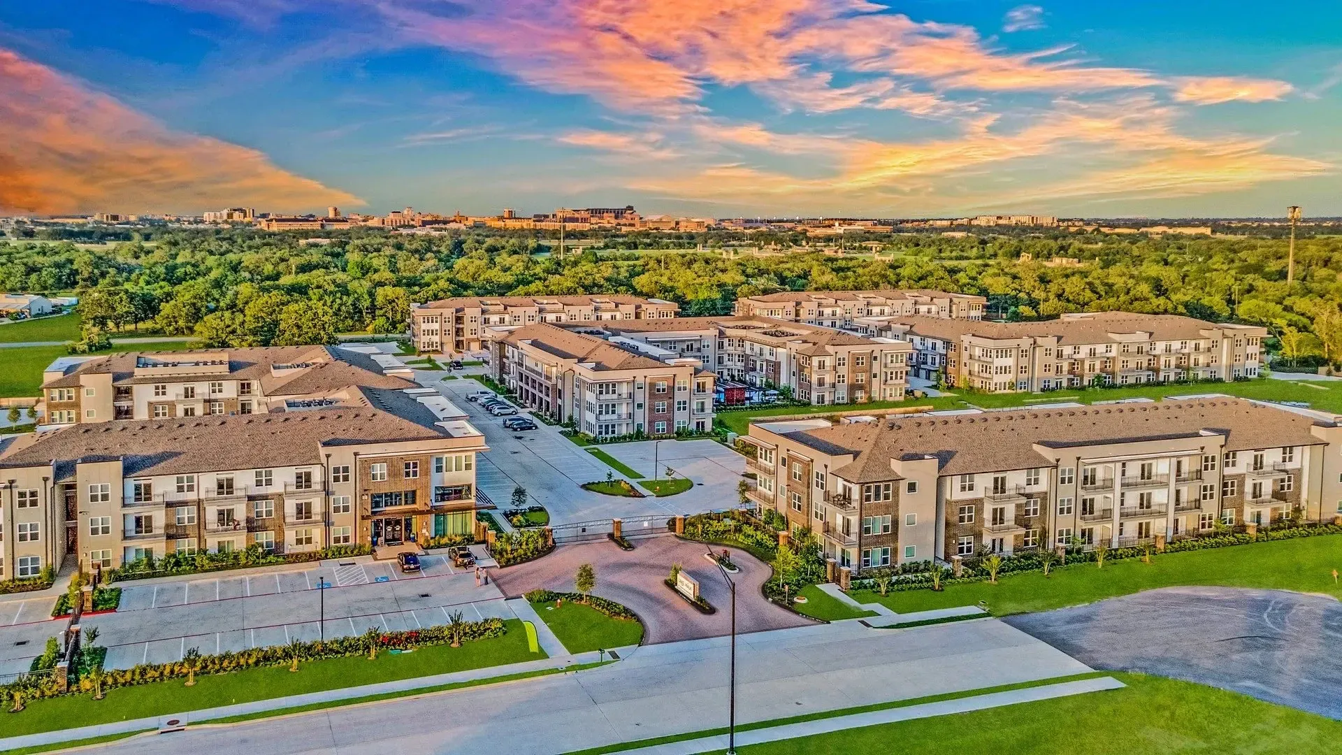 Aerial view of a modern apartment complex surrounded by green trees and blue sky.