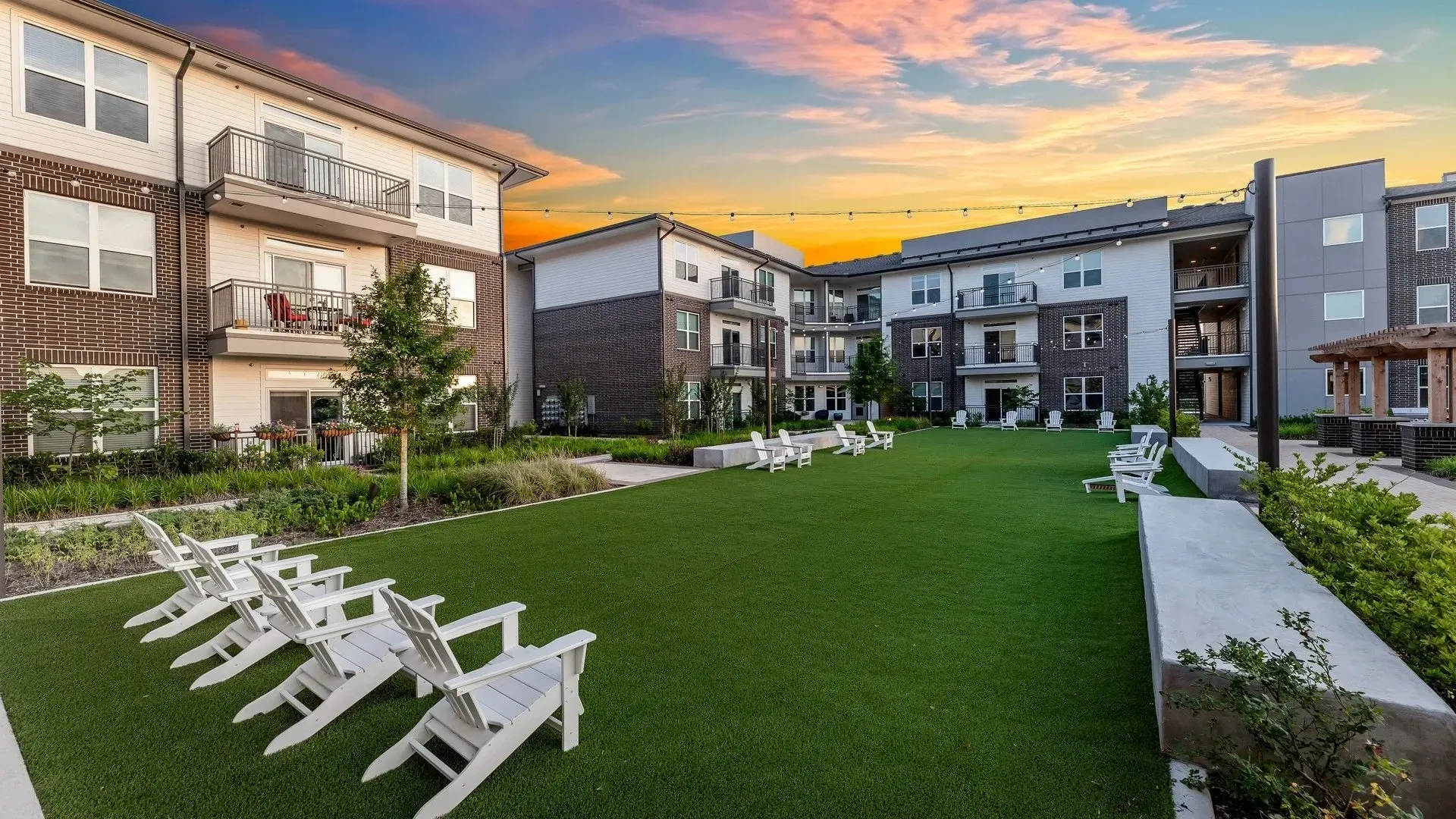 View of a landscaped green area with seated space in front of residential buildings.