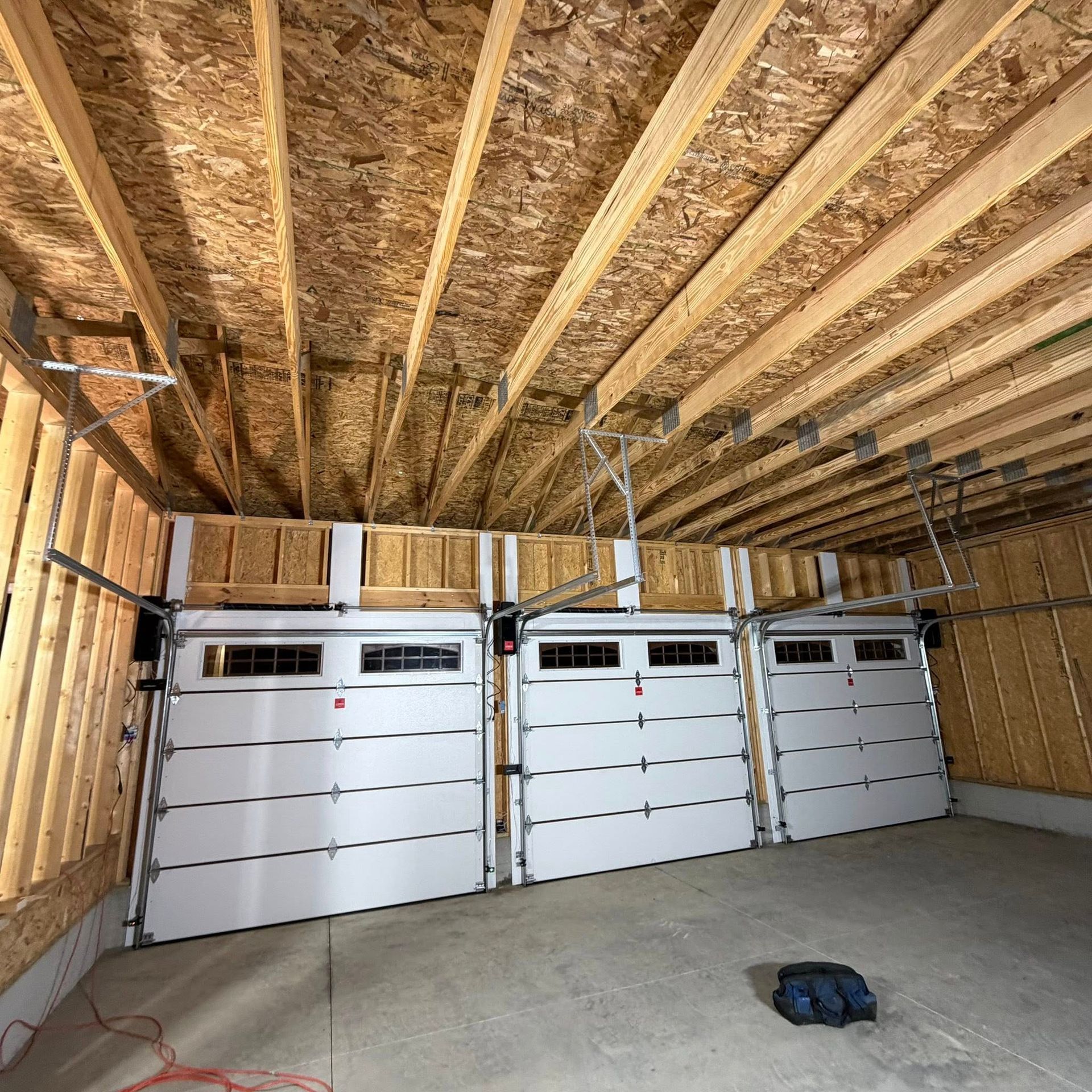 Three white garage doors inside a garage under construction with exposed wooden framing.