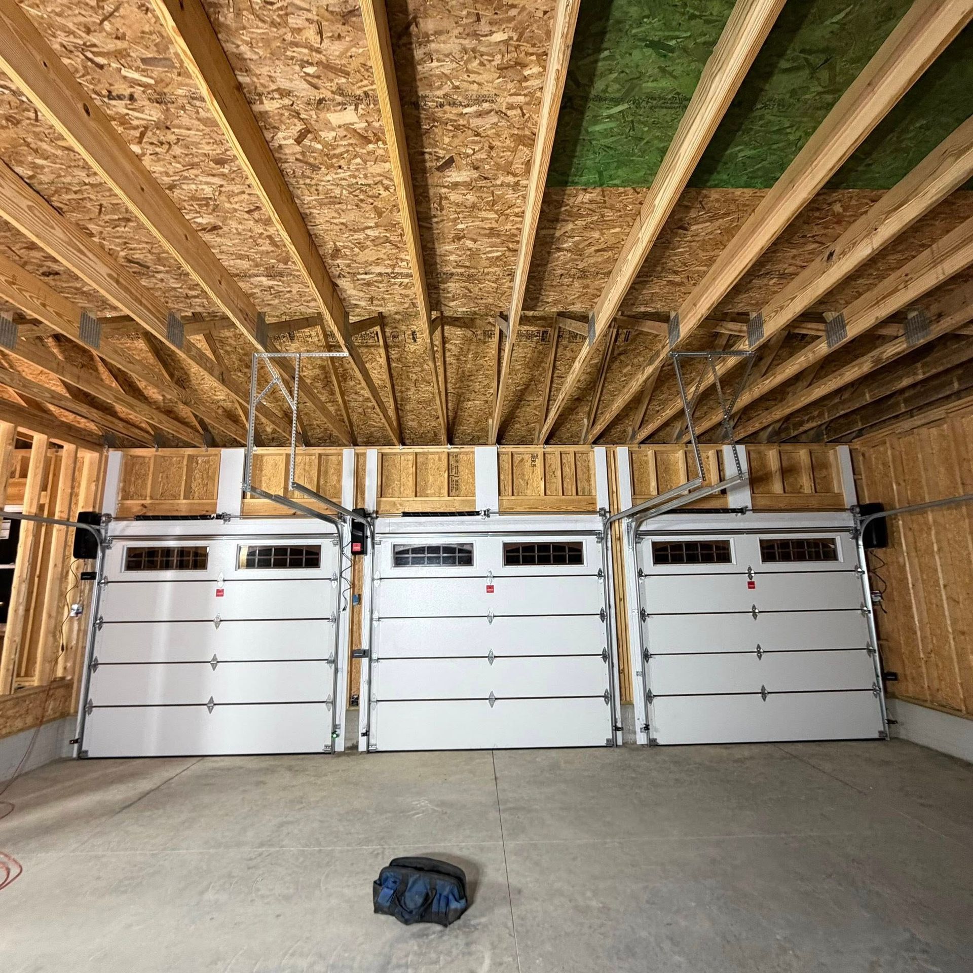 Interior view of a garage with three white garage doors. The doors are closed. Wooden beams and ceiling are visible.