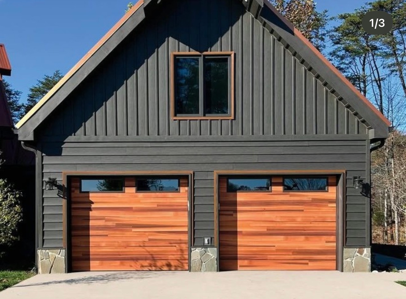 Two-car garage with wood-paneled doors, gray siding, and a small window above.