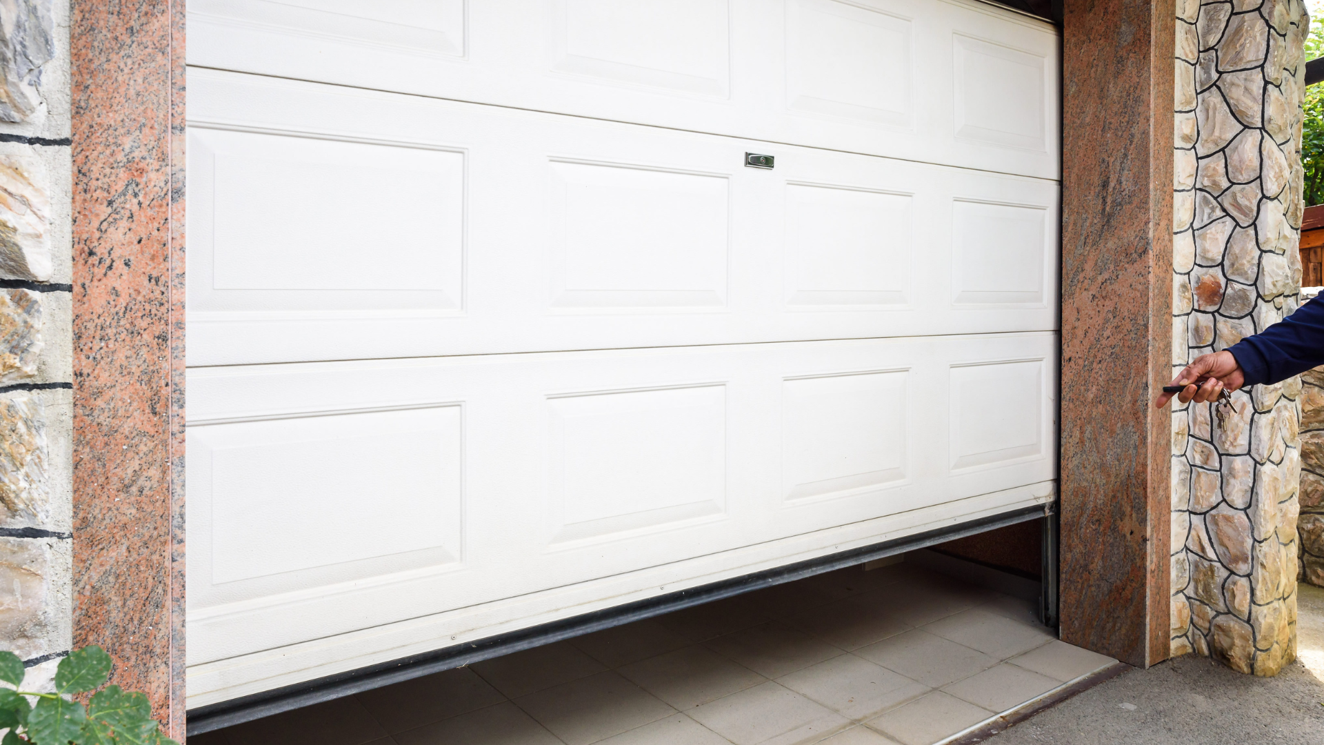 White garage door opening, person's hand holding a remote, stone siding.