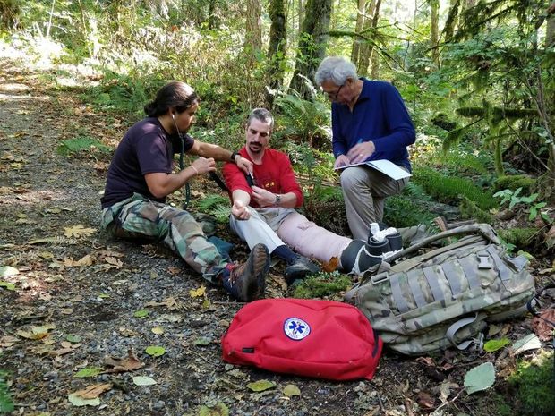 A man with a bandage on his leg is sitting on the ground in the woods.