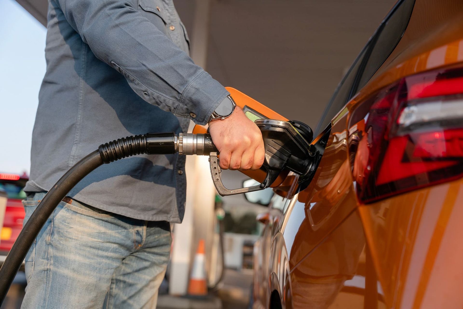 Person pumping gas into an orange car at a gas station.