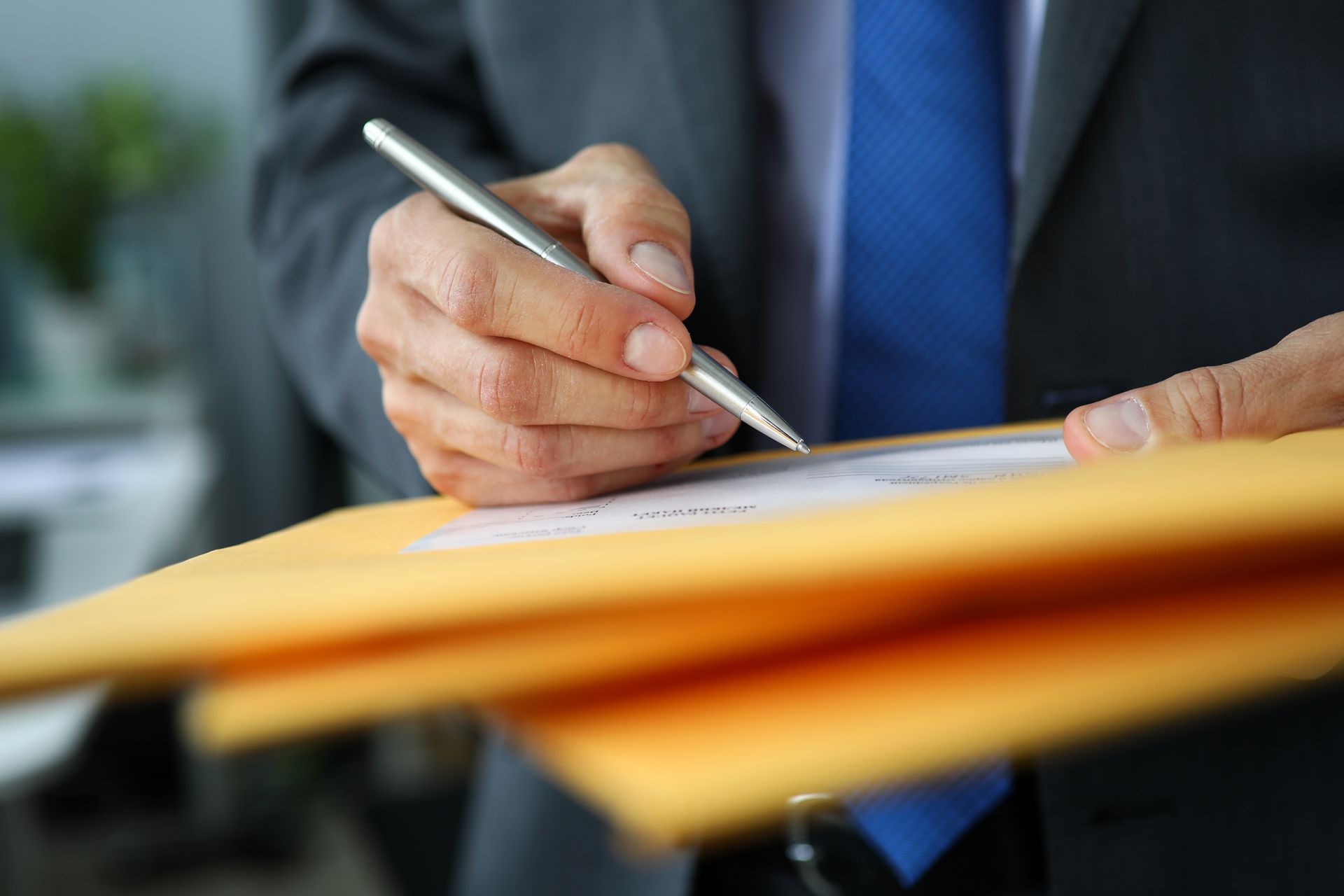 Person in suit signing document on an envelope. Blue tie, silver pen.