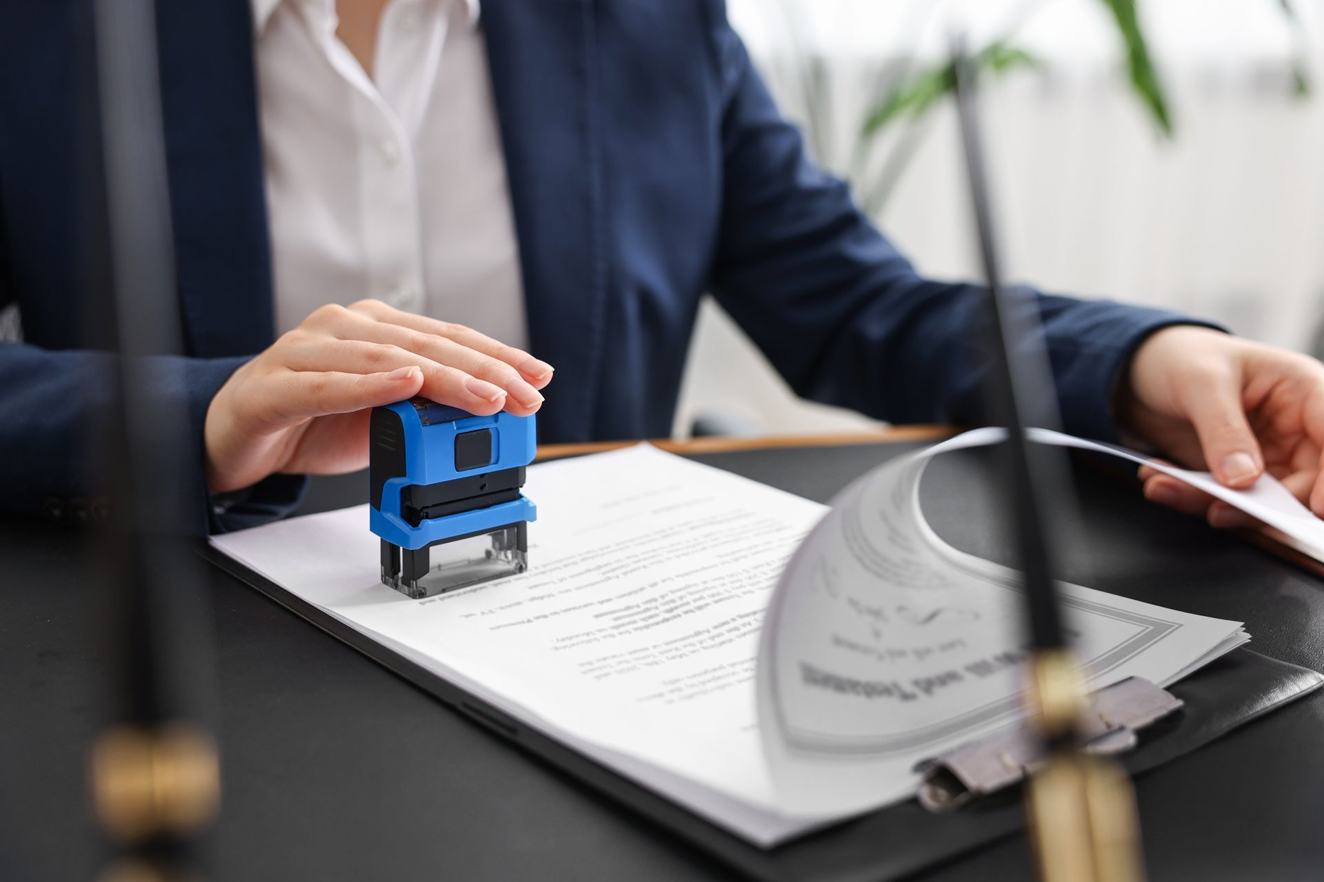 Person in a suit stamps a document with a blue stamp on a black desk.
