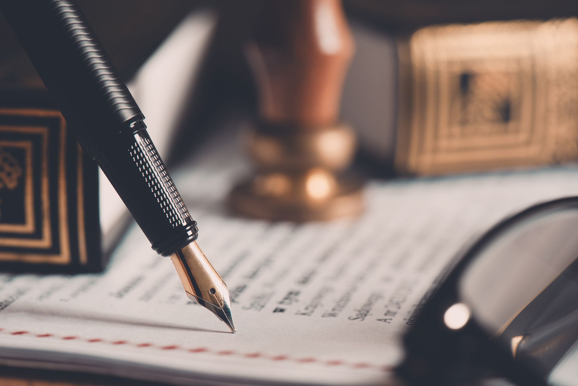 Fountain pen on document, with a stamp and glasses in background. Legal setting.
