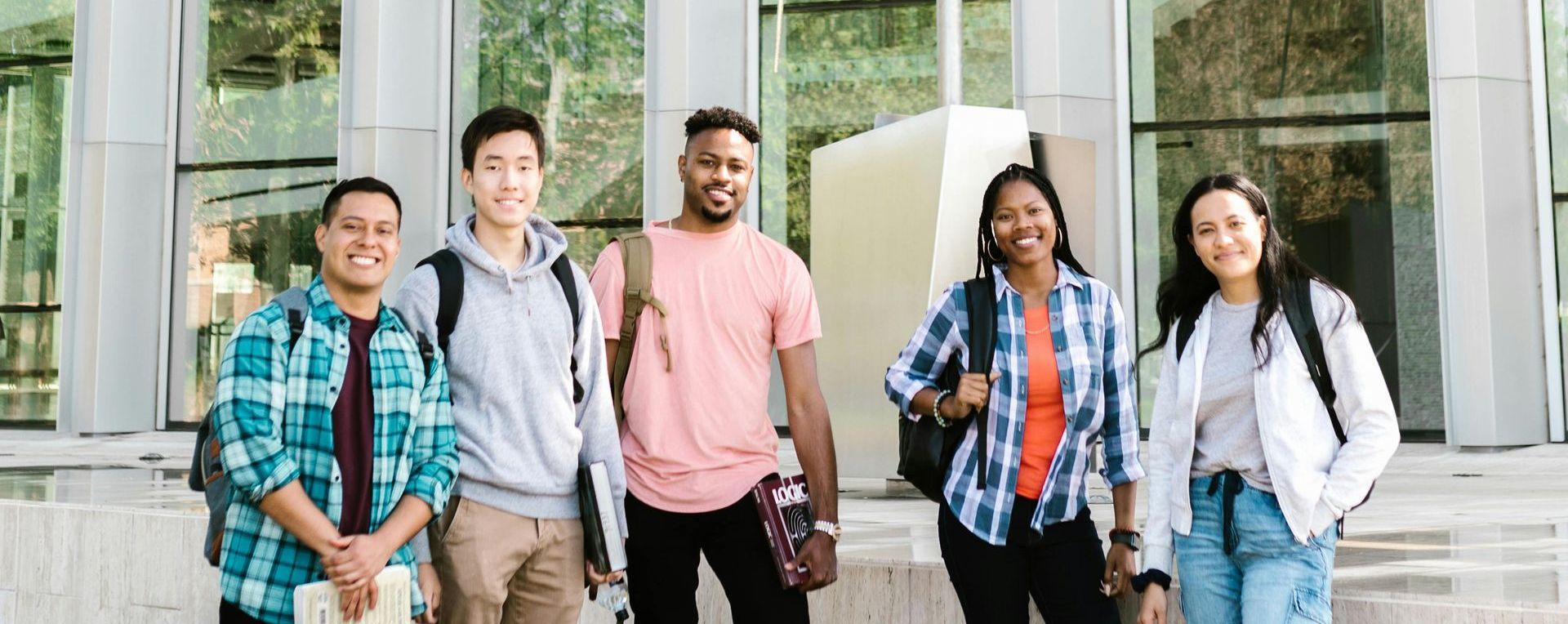 Group of five diverse students smiling in front of a modern building.