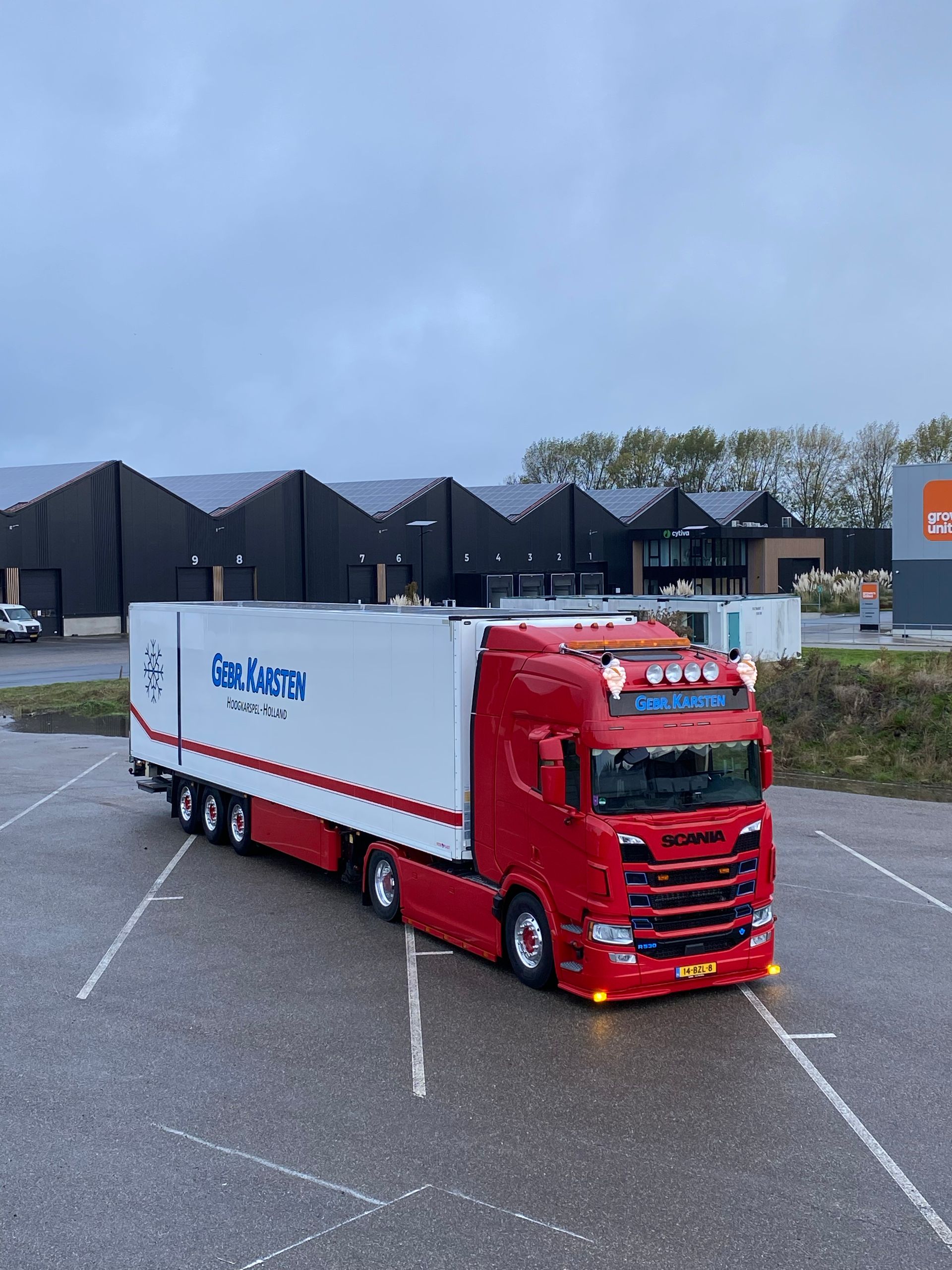 Rood-witte vrachtwagen geparkeerd op een parkeerplaats; bewolkte lucht.