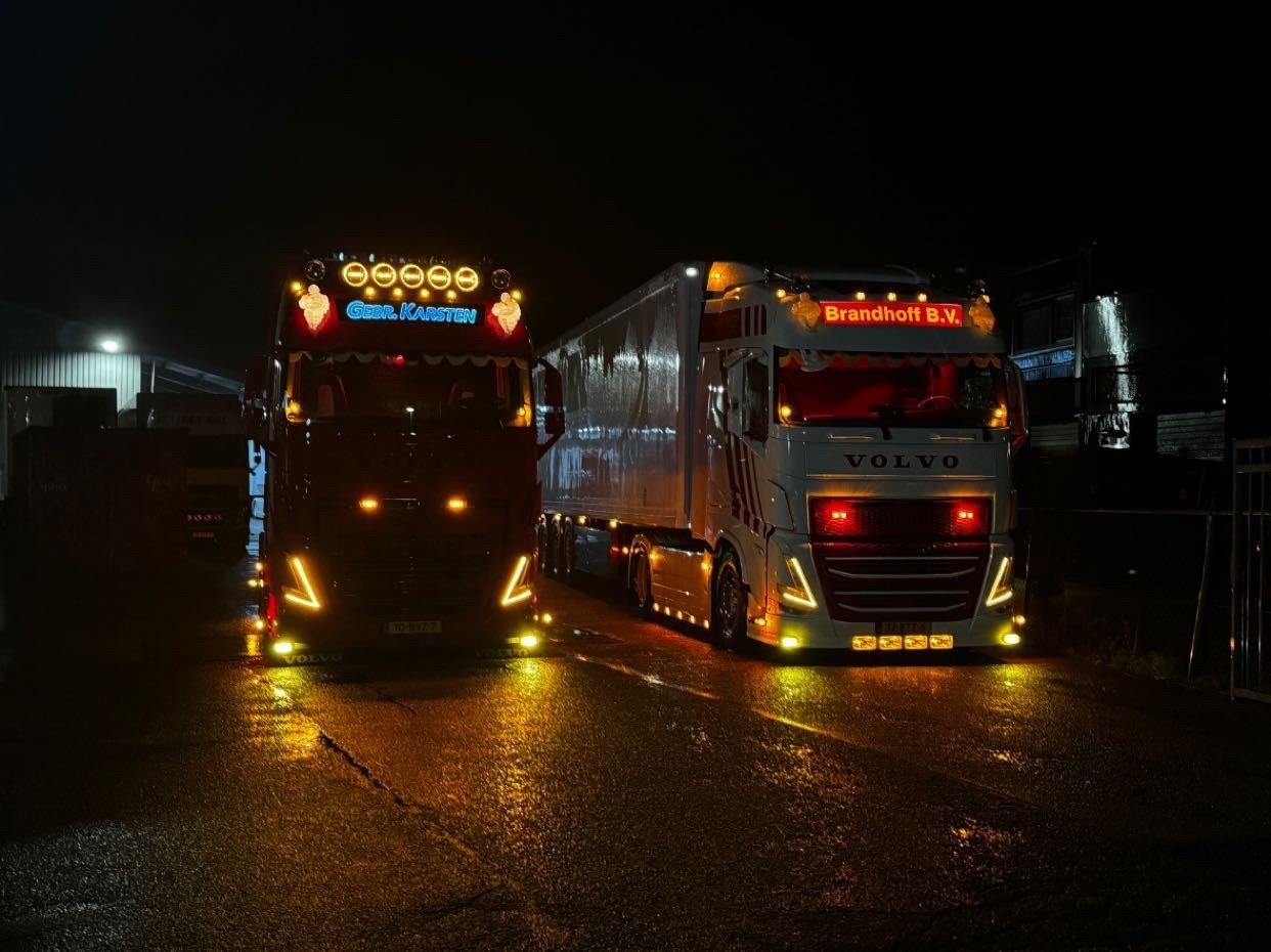 Gebr-Karsten-Transport vrachtwagens ’s nachts geparkeerd met felle lichten die reflecteren op nat wegdek
