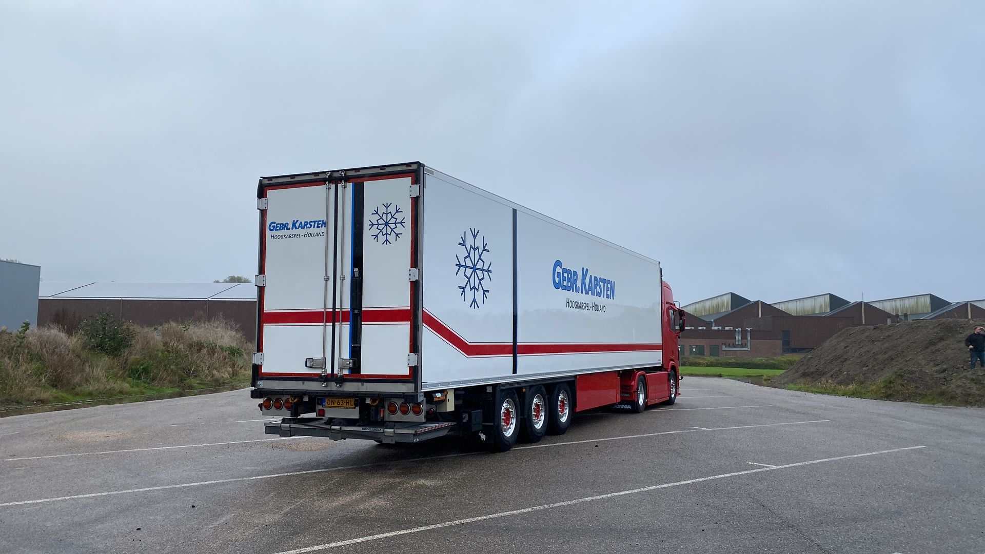 Witte vrachtwagen met oplegger en blauwe en rode details, geparkeerd op asfalt op een bewolkte dag.