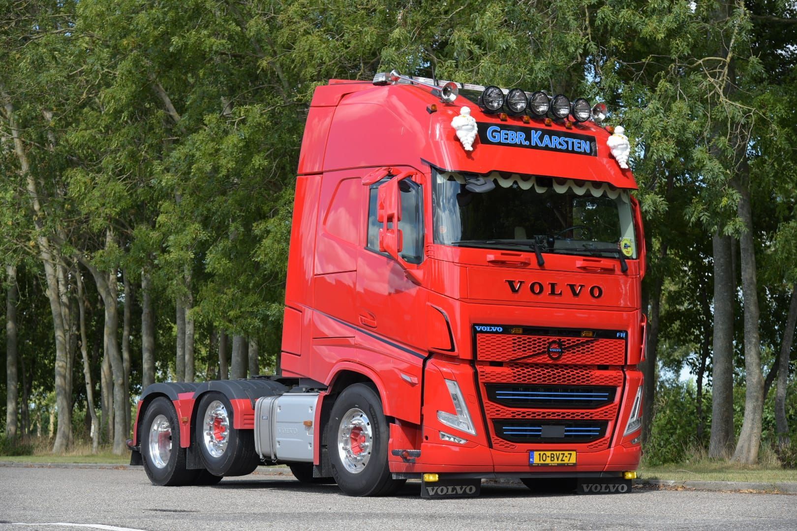 Rode Volvo-vrachtwagen geparkeerd buiten. Hij heeft meerdere wielen, een speciale grille en lampen op het dak.