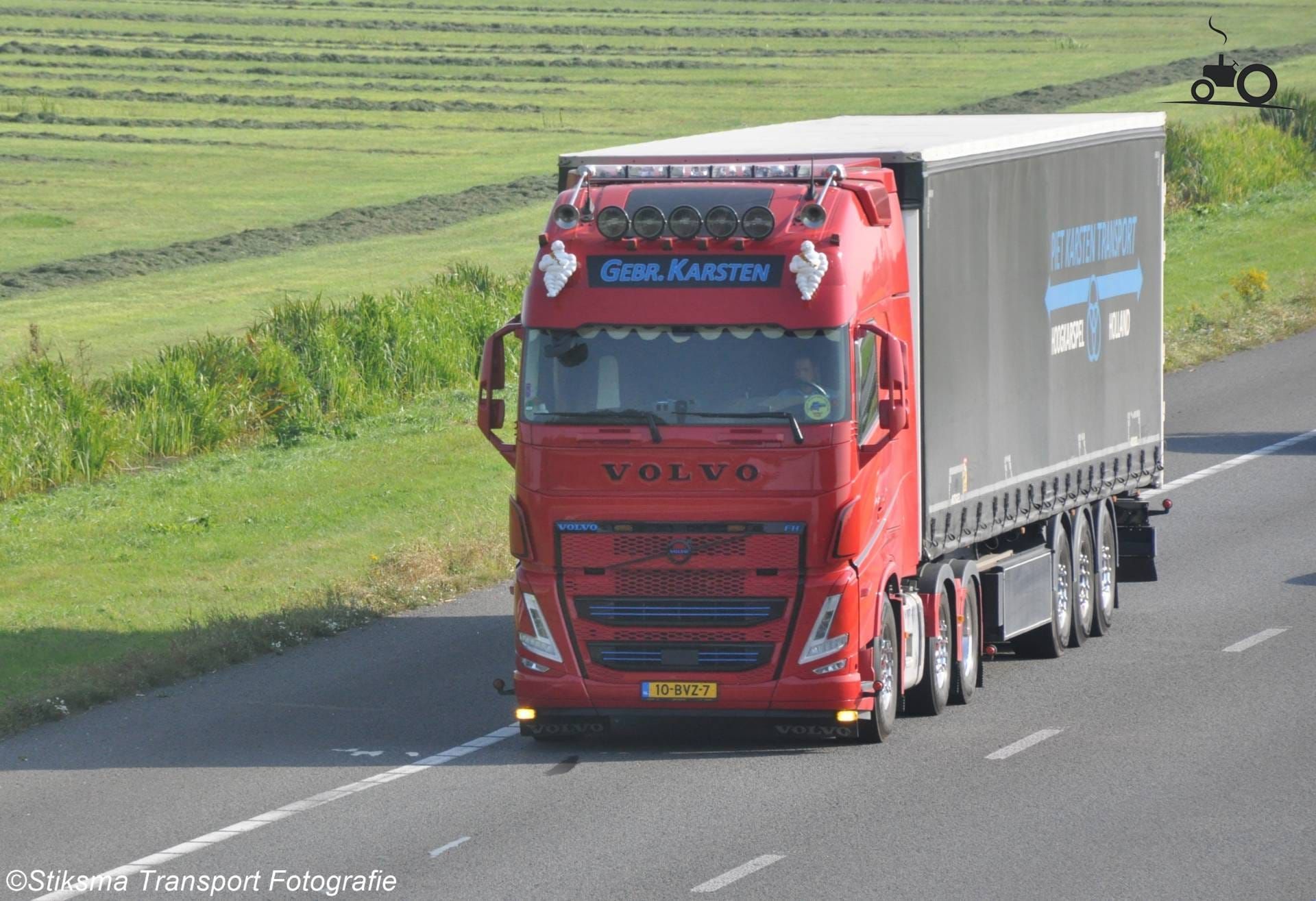 Rode Volvo-vrachtwagen op de snelweg met een aanhanger. Groene velden op de achtergrond.