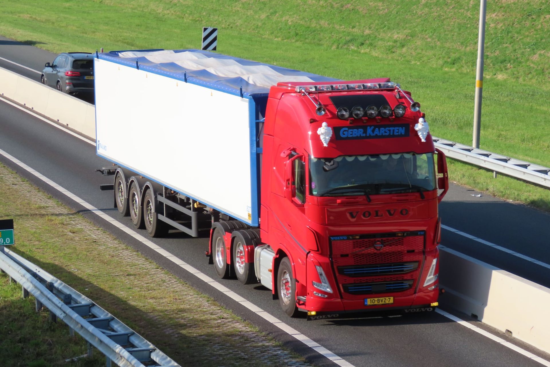 Rode Volvo-vrachtwagen op de snelweg met een wit-blauwe oplegger.