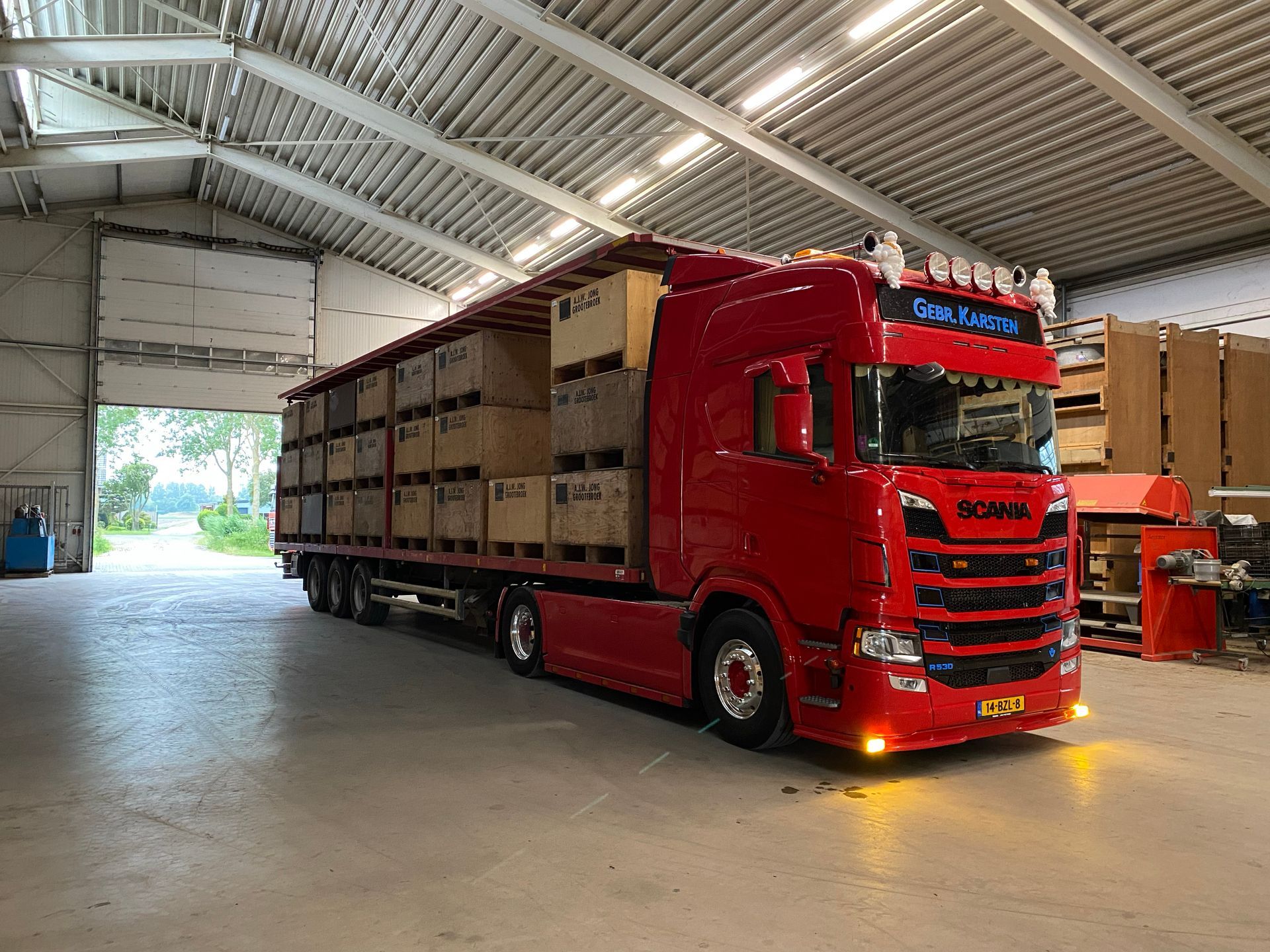gebr-karsten-transport rode vrachtwagen met dozen in loods, felle verlichting en open loodsdeur
