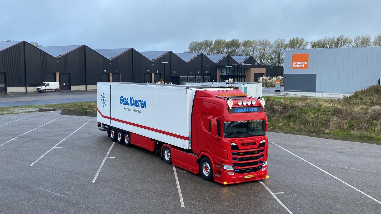 Rood-witte vrachtwagen op een parkeerplaats. Gebouwen op de achtergrond. Vrachtwagen met bedrijfslogo.