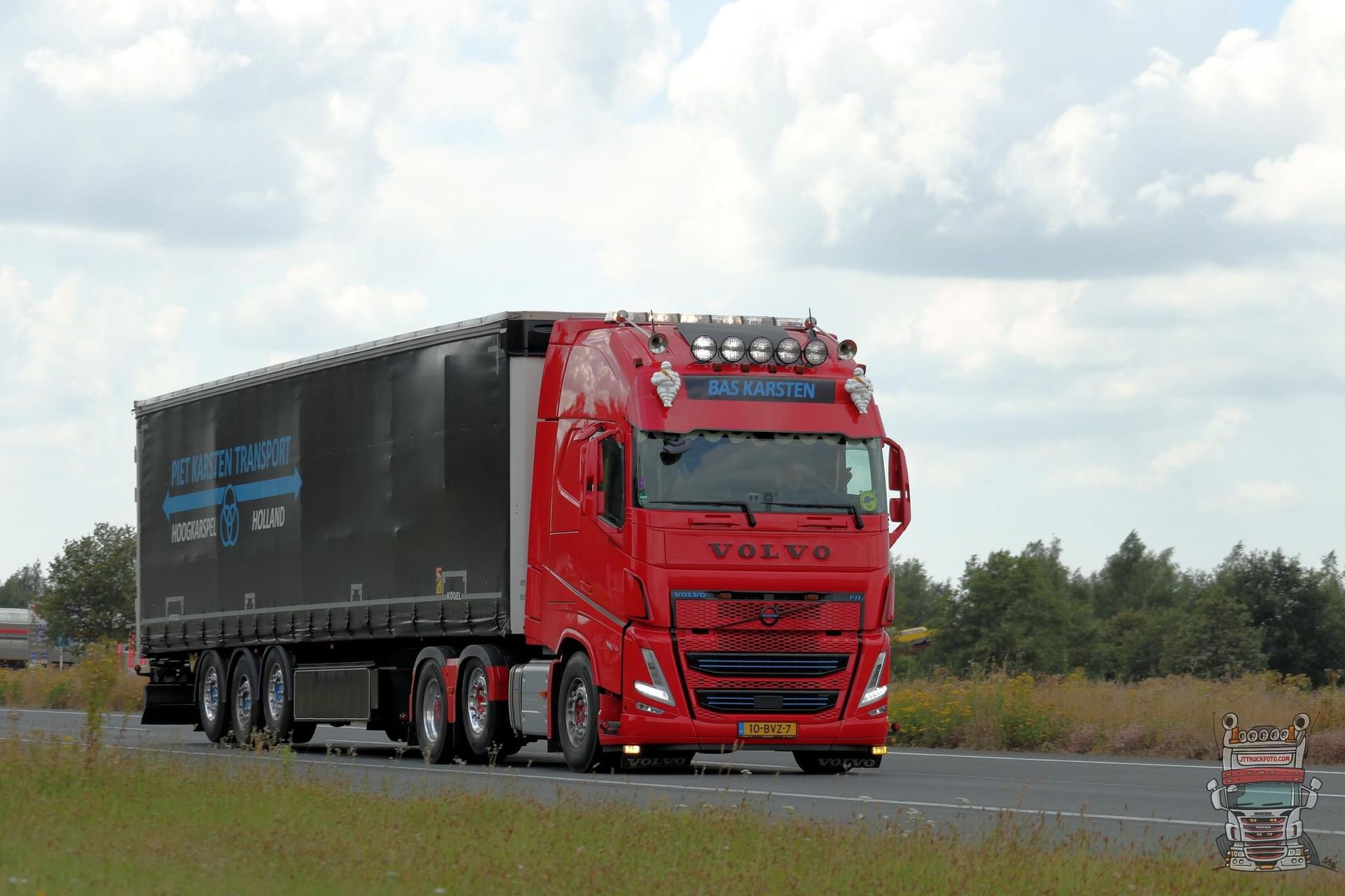 Rode Volvo vrachtwagen met donkere oplegger, rijdend op de weg.