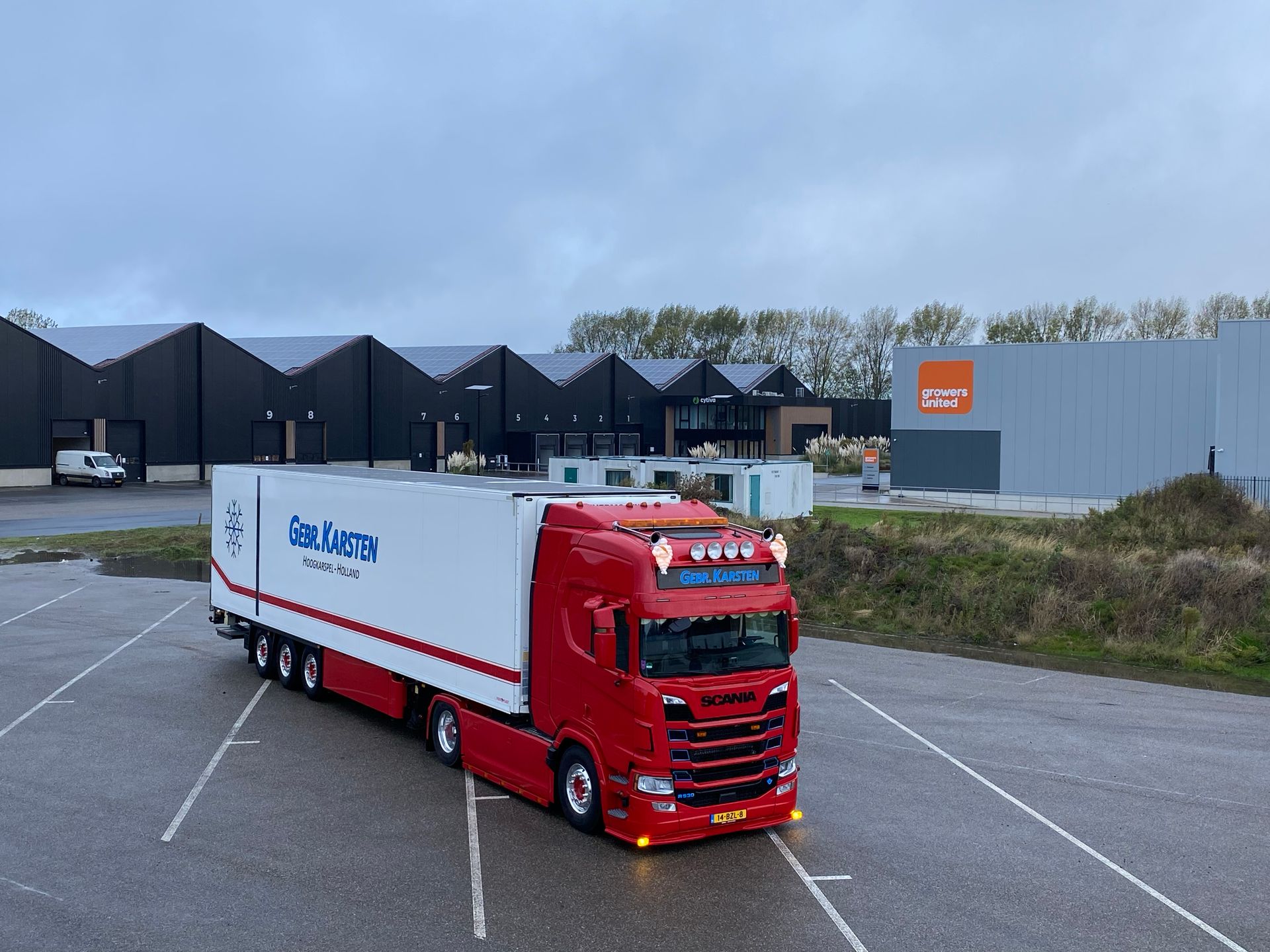Rode vrachtwagen op een parkeerplaats, voor gebouwen, onder een bewolkte lucht.