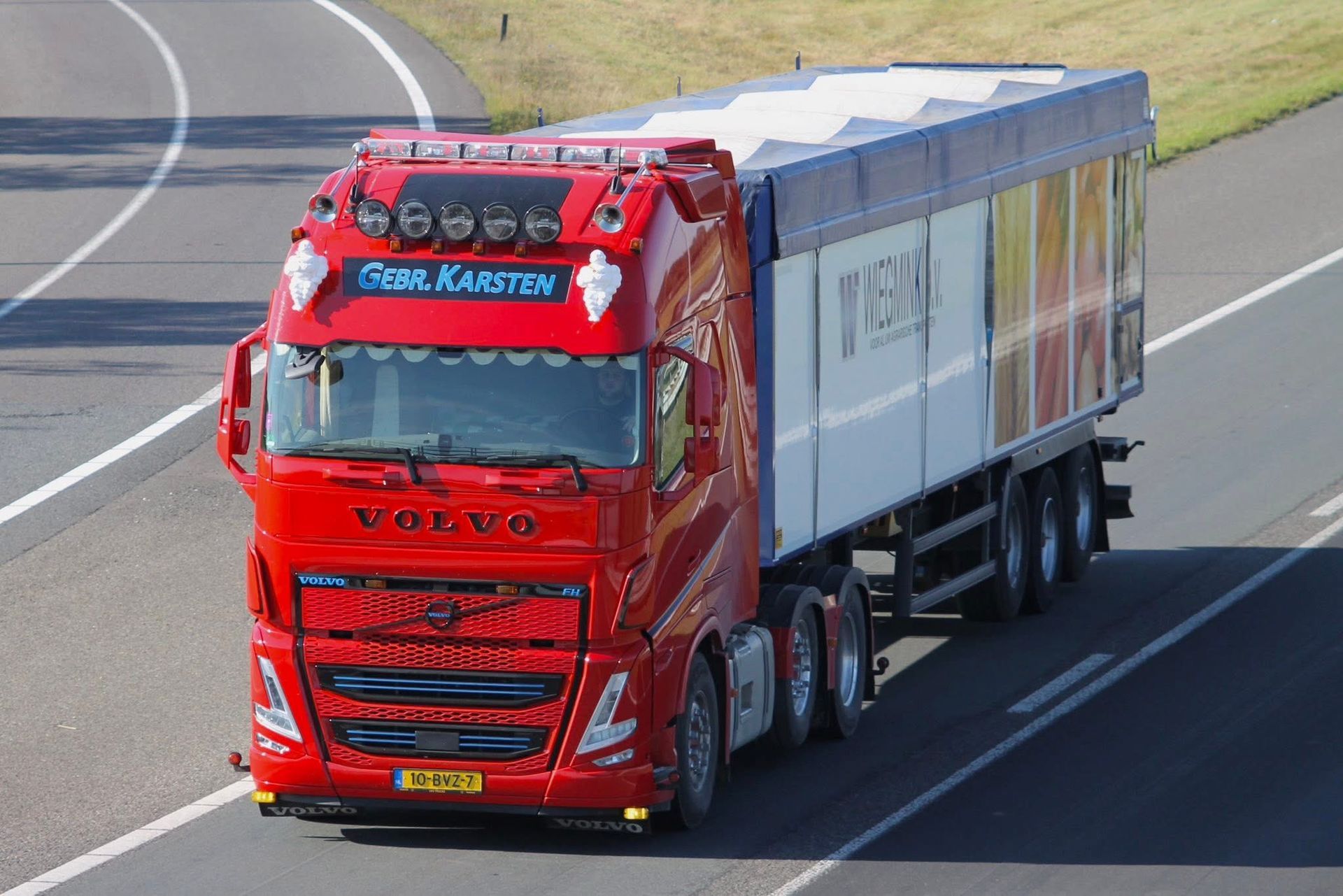 Rode Volvo-vrachtwagen met wit-blauwe oplegger rijdt op de snelweg.