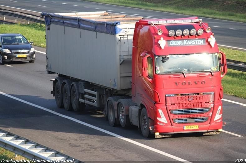 Rode Volvo-vrachtwagen met containeroplegger rijdt op de snelweg.
