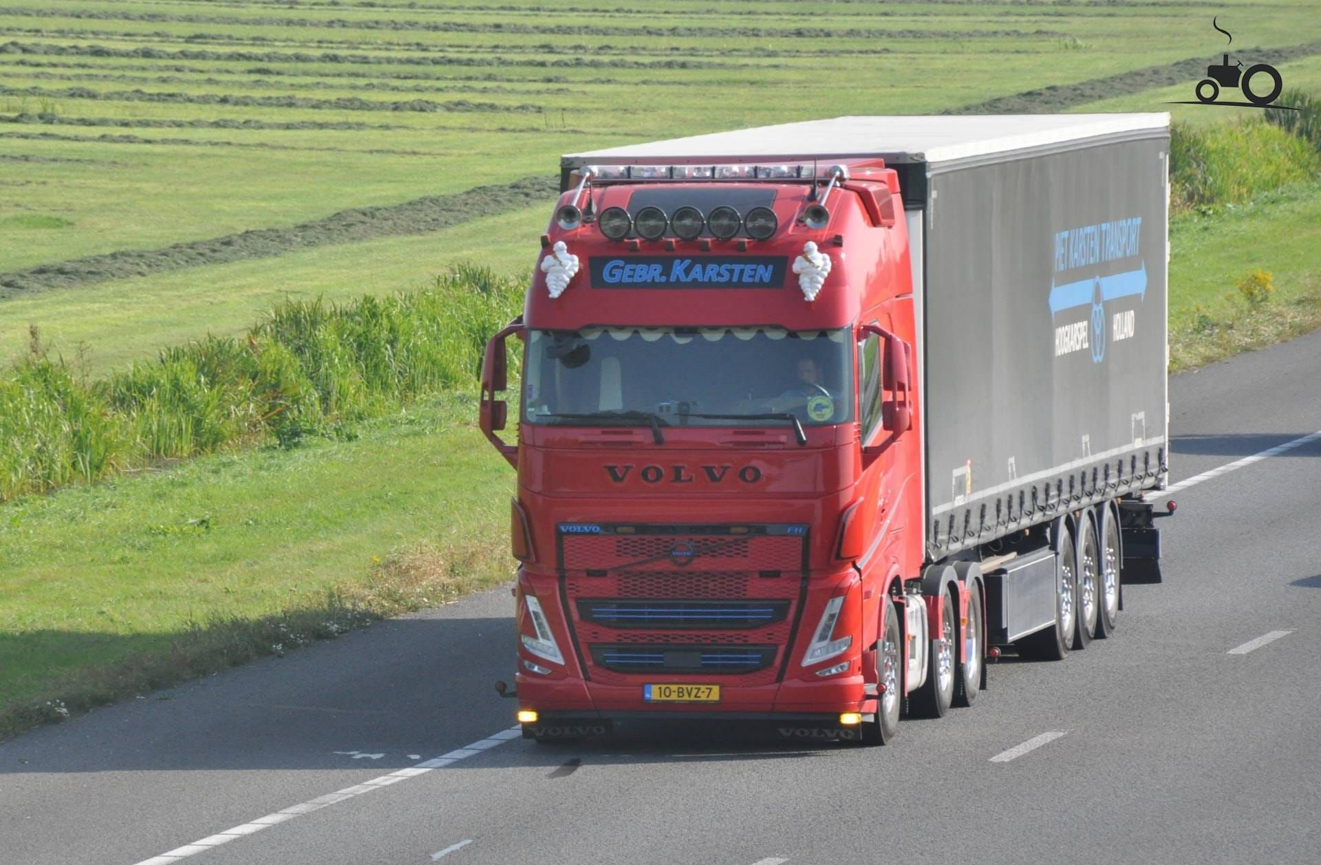Rode Volvo-vrachtwagen met aanhanger rijdt op de snelweg.