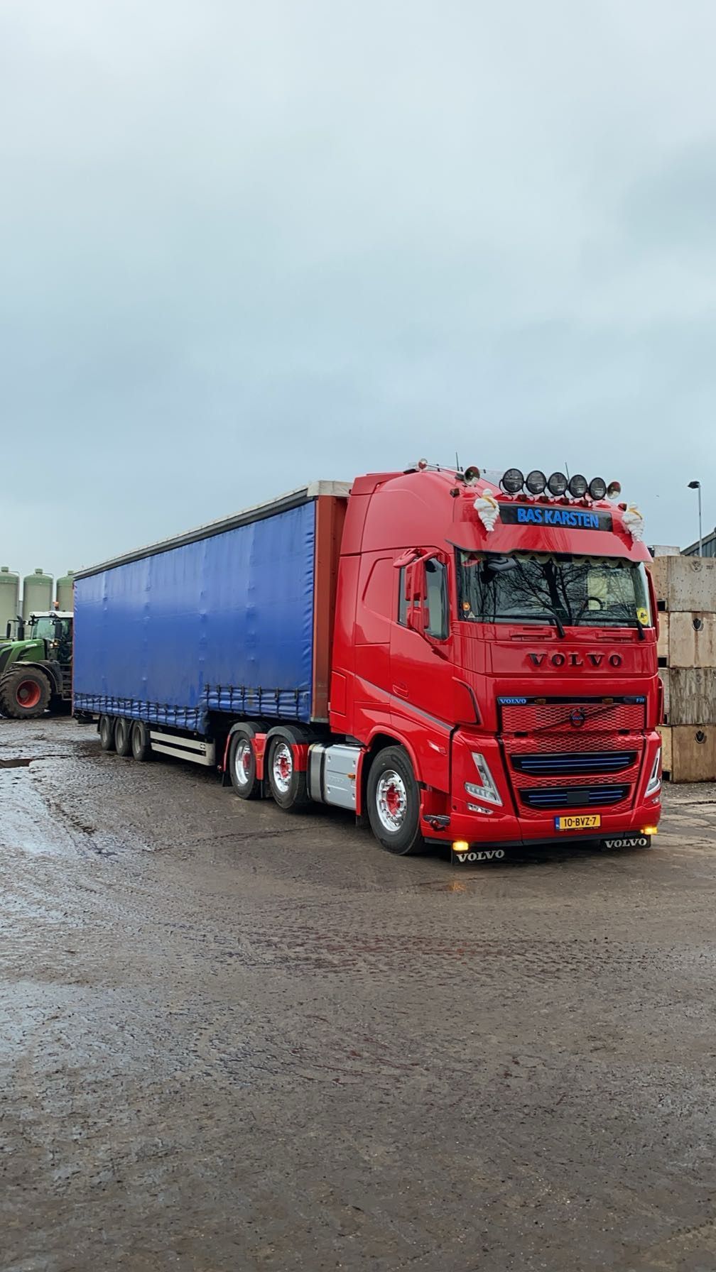 Rood-blauwe Volvo vrachtwagen met oplegger op natte grond. Bewolkte dag.