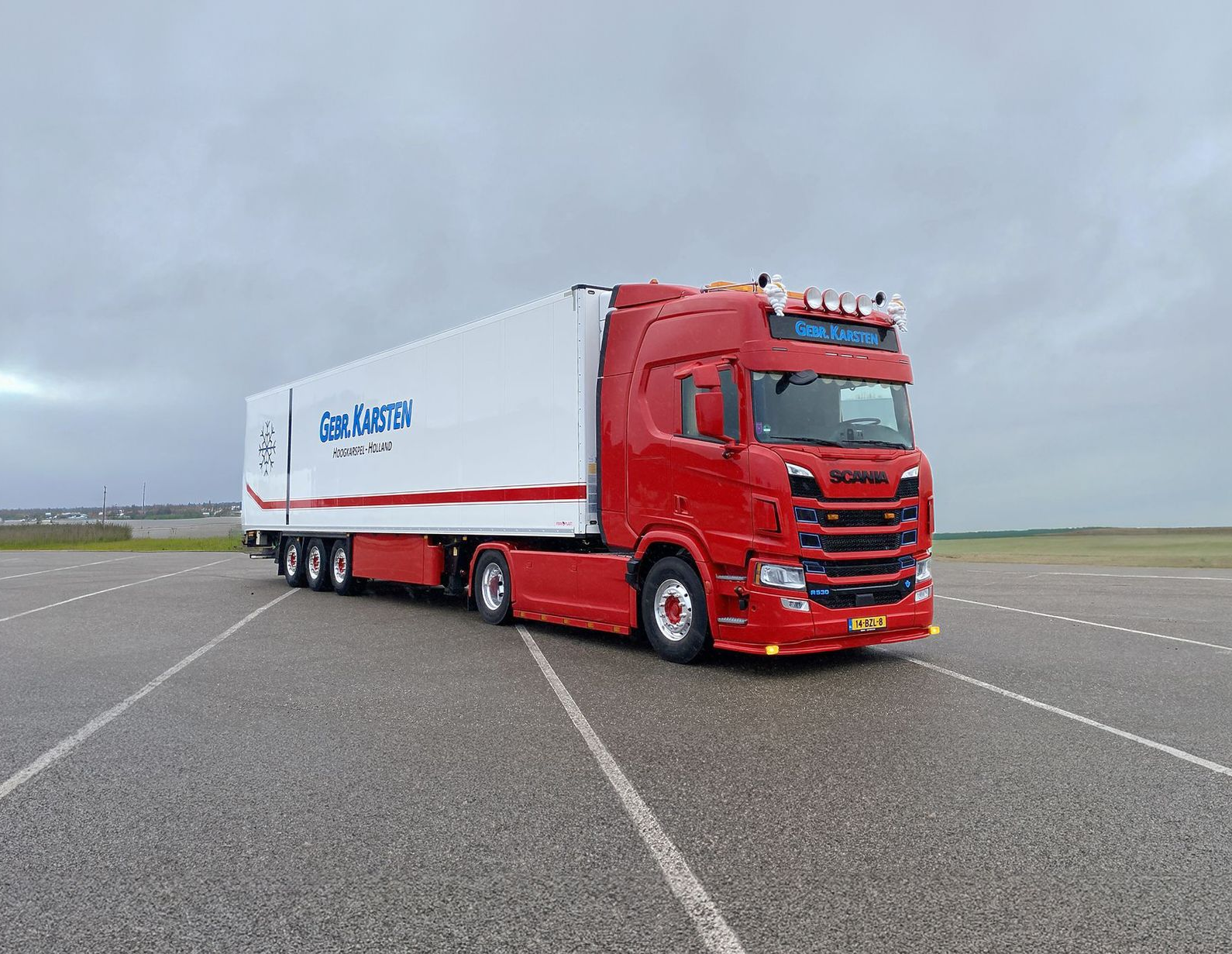 Rood-witte vrachtwagen op asfaltweg onder bewolkte hemel met het Gebr. Karsten-logo zichtbaar