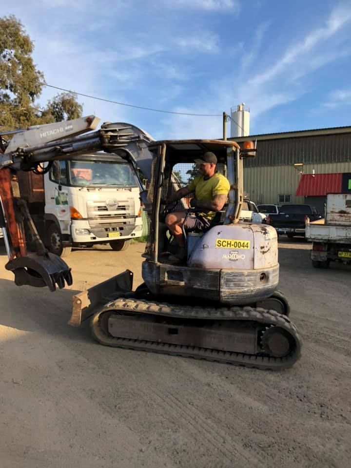A Man Is Driving A Small Excavator On A Dirt Road — RiverCity Recyclers In Port Macquarie, NSW