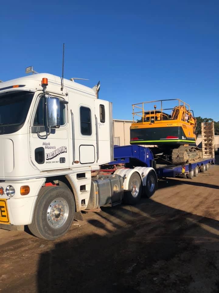 A White Semi Truck Is Carrying A Yellow Excavator On A Trailer — RiverCity Recyclers In Taree, NSW