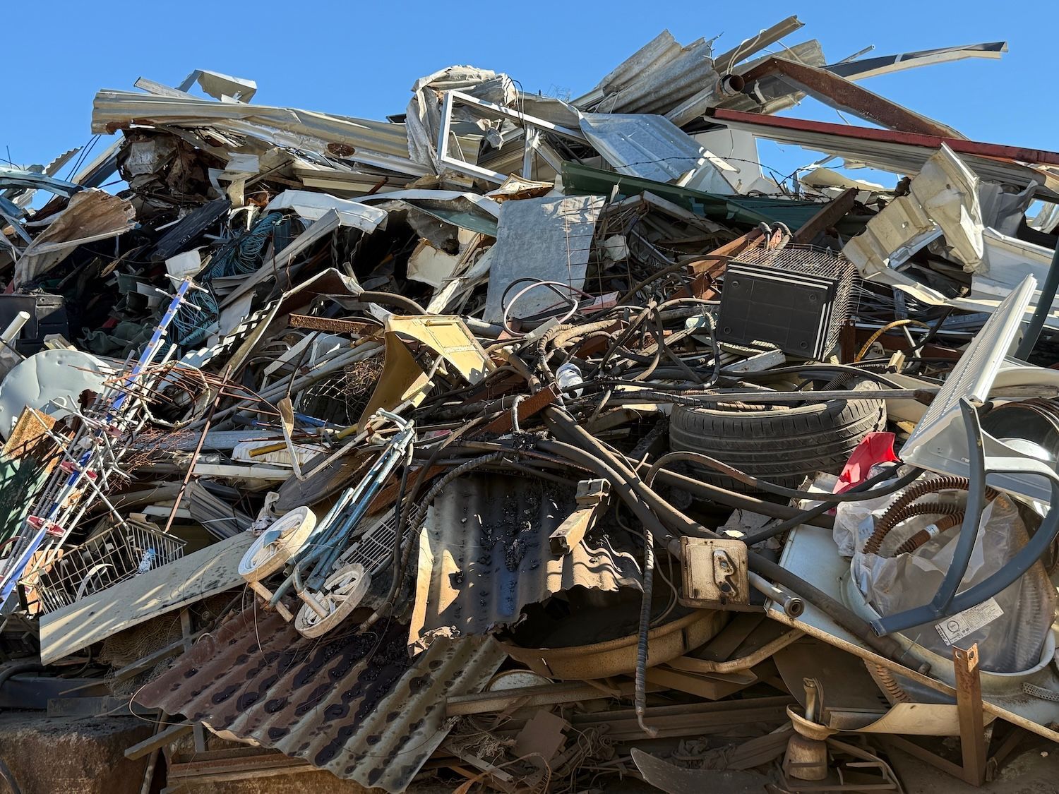 Pile of twisted metal and debris at a demolition site under a clear blue sky