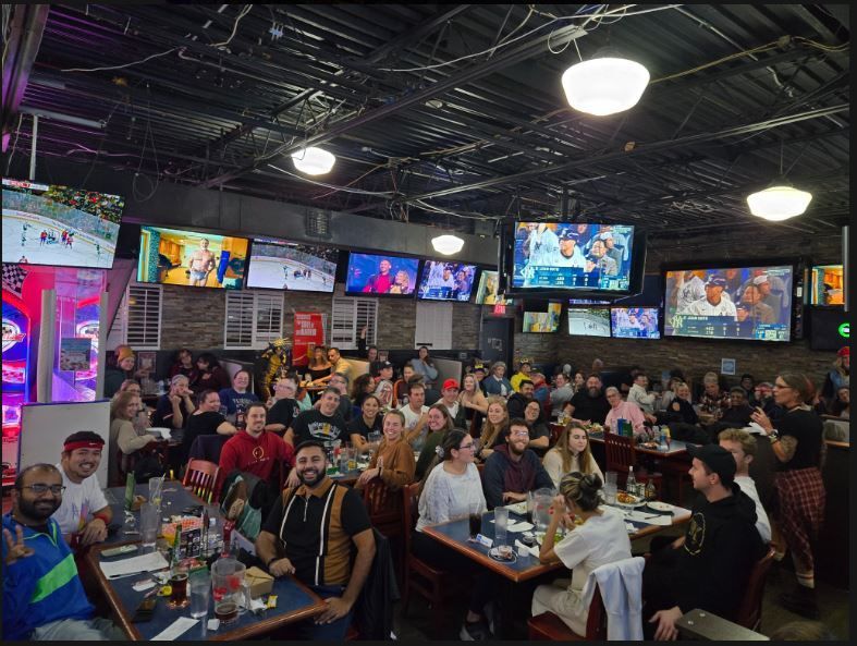 A large group of people are sitting at tables in a restaurant watching a game.