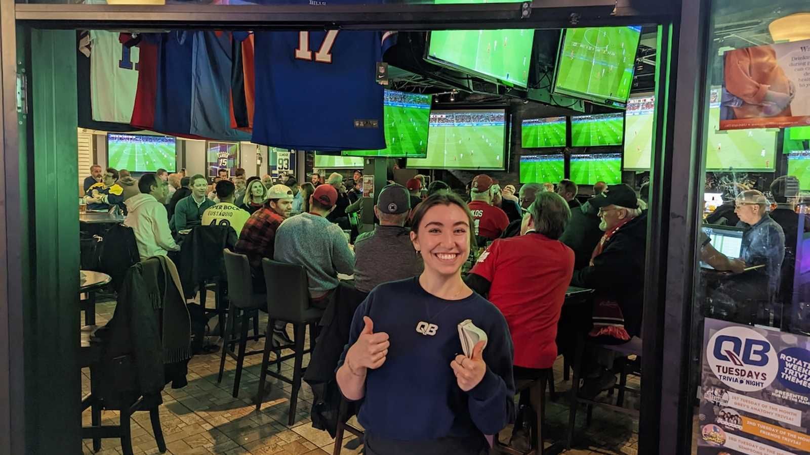 A woman is standing in front of a crowd of people in a bar.