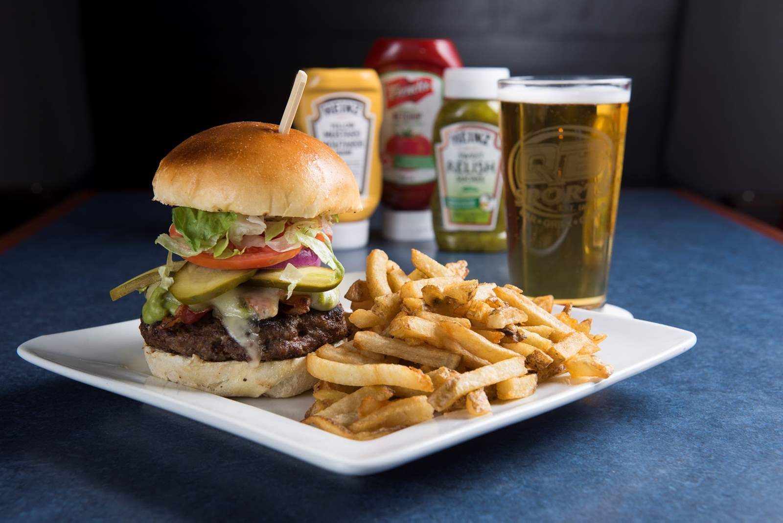 A hamburger and french fries on a white plate next to a glass of beer.