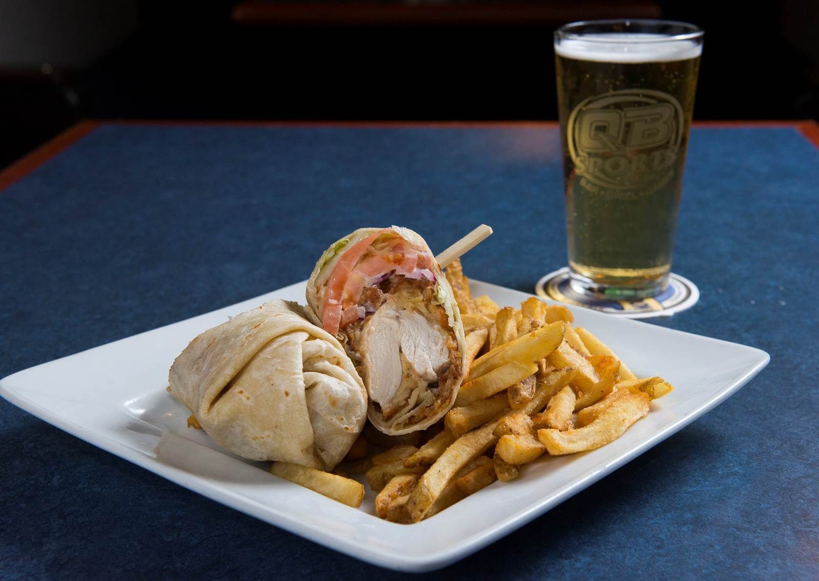 A white plate topped with a wrap and french fries next to a glass of beer.