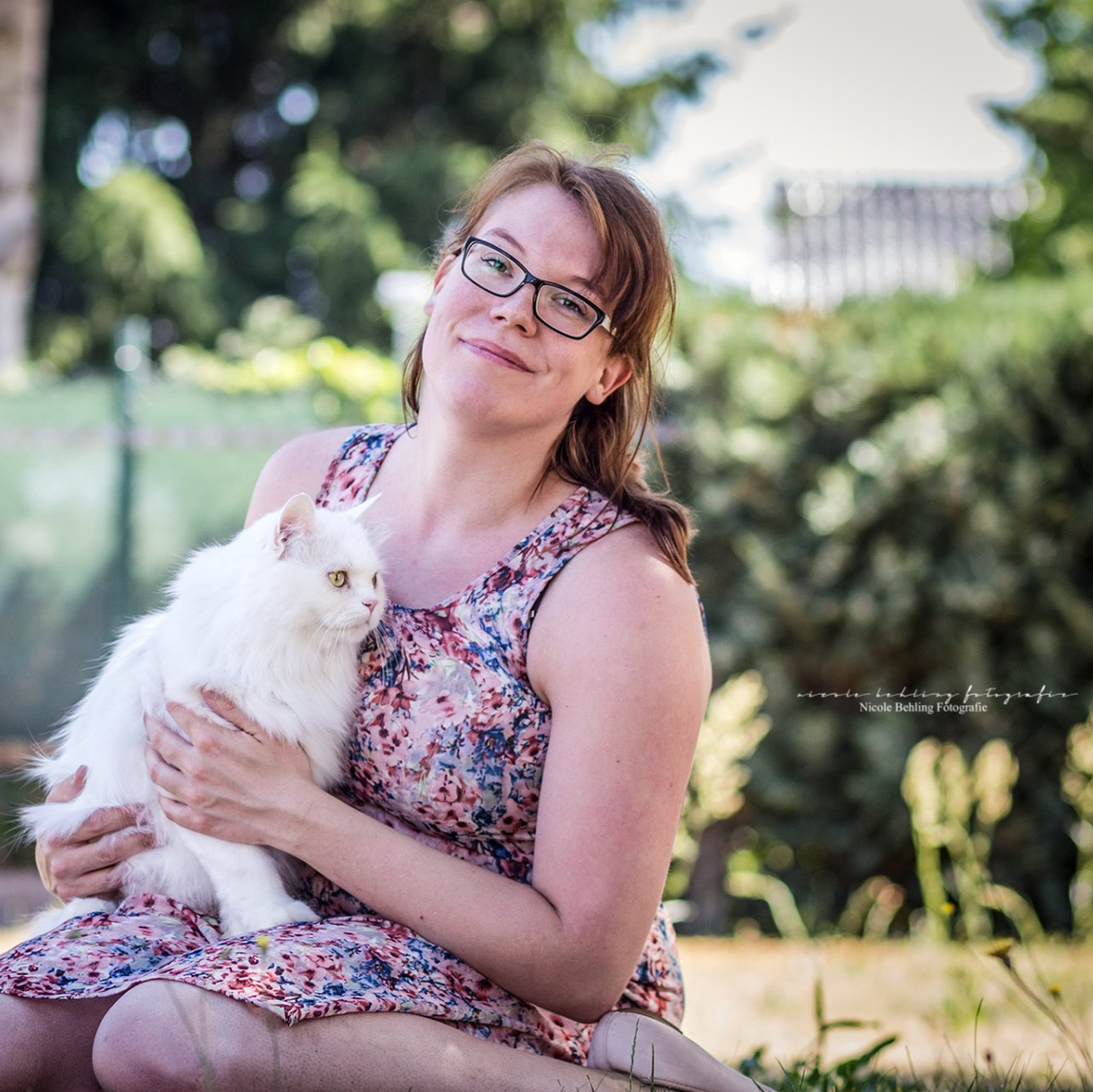 Eine Frau in einem geblümten Kleid hält eine weiße Katze