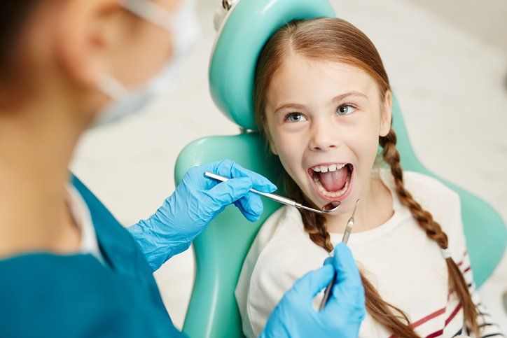 A little girl is sitting in a dental chair getting her teeth examined by a dentist.