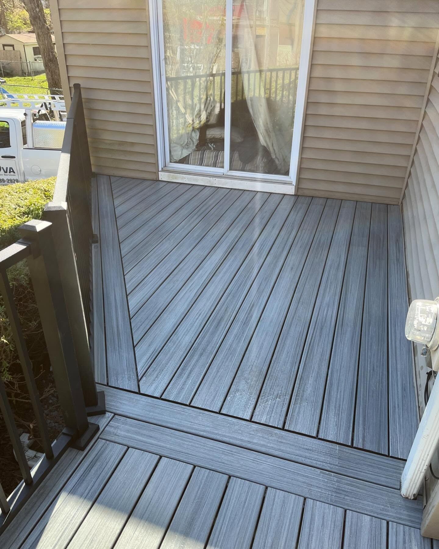 Gray composite deck outside a house, with a sliding glass door visible.
